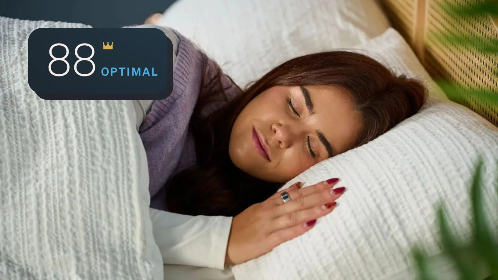 Our sleep tech tester wearing the silver Oura Ring 4 on left index finger sleeping in bed with white sheets on her side, with inset of Oura sleep score of 88